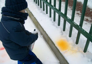 Dzieci wyposażone w spryskiwacze do wody z kolorowymi barwnikami tworzą na śniegu kolorowe obrazy